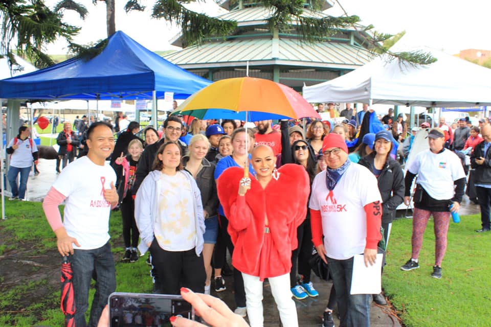 Group of people posing for a photo at an outdoor event, one holding a colorful umbrella.