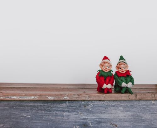 Two christmas elf decorations sitting on a wooden surface against a white background.