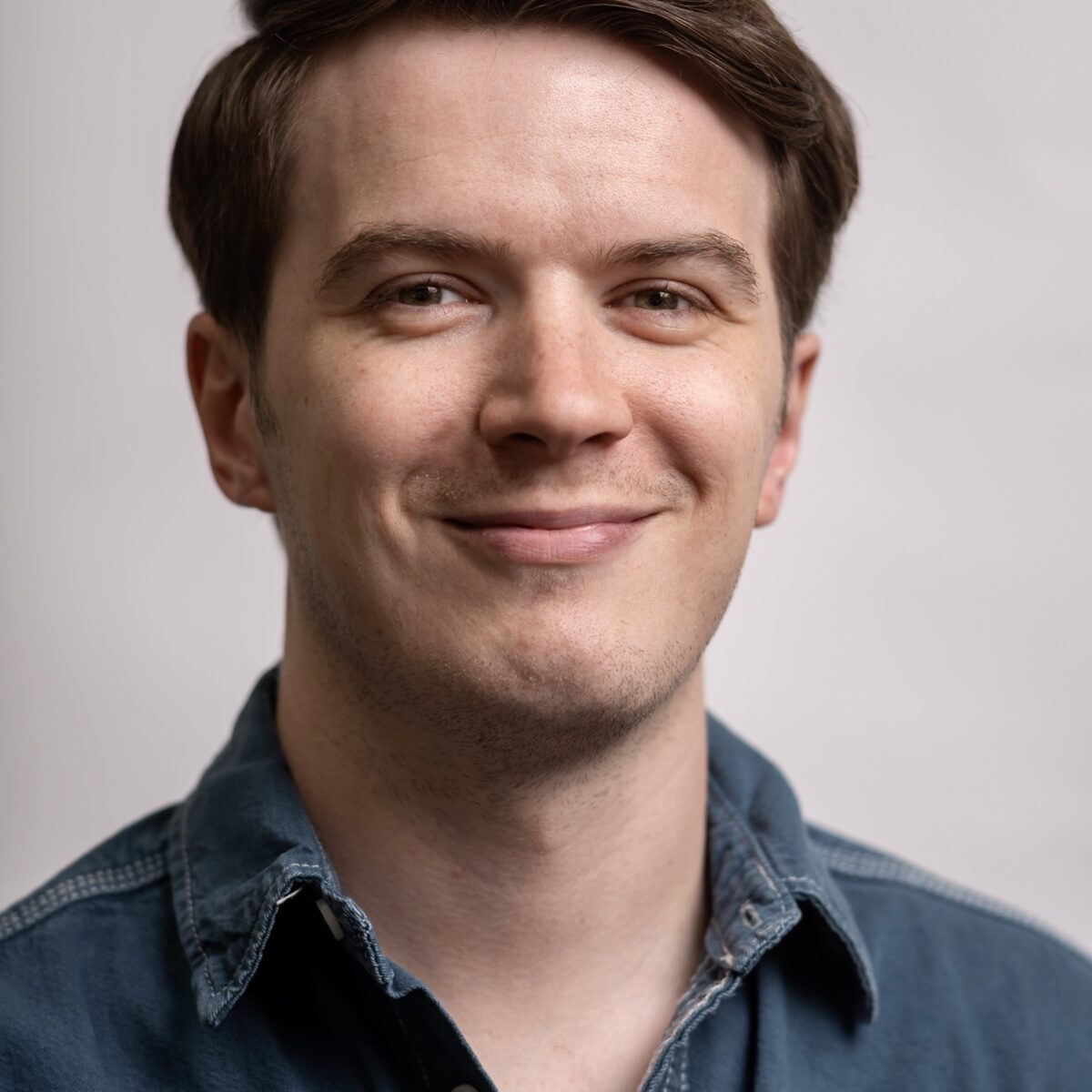 A smiling man in a blue shirt against a pale background.